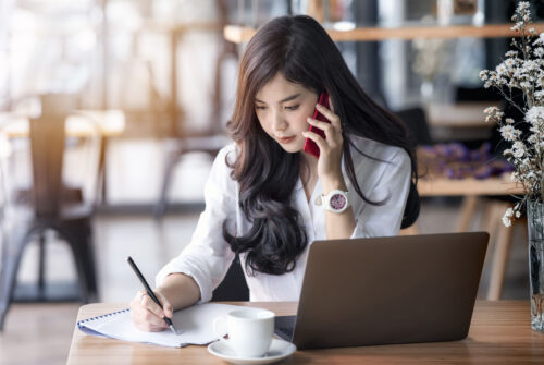young asian business woman using laptop and writing on notebook, woman officer hard working communicate with customer and record